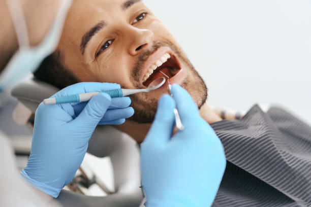 Smiling young man sitting in dentist chair while doctor examining his teeth