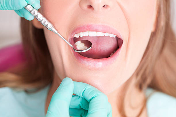 Female patient with open mouth receiving dental inspection at dentist's office