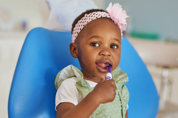 Shot of an adorable little girl brushing her teeth in a dentist’s chair